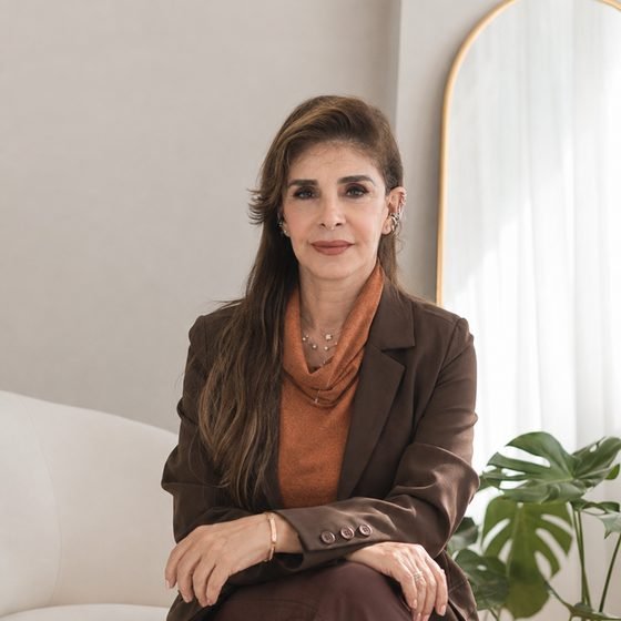 Dra. Zarifa Khoury sentada em uma poltrona clara, em sala iluminada